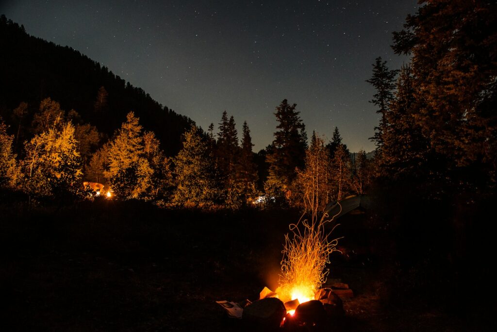 Campsite glowing by firelight under a night sky